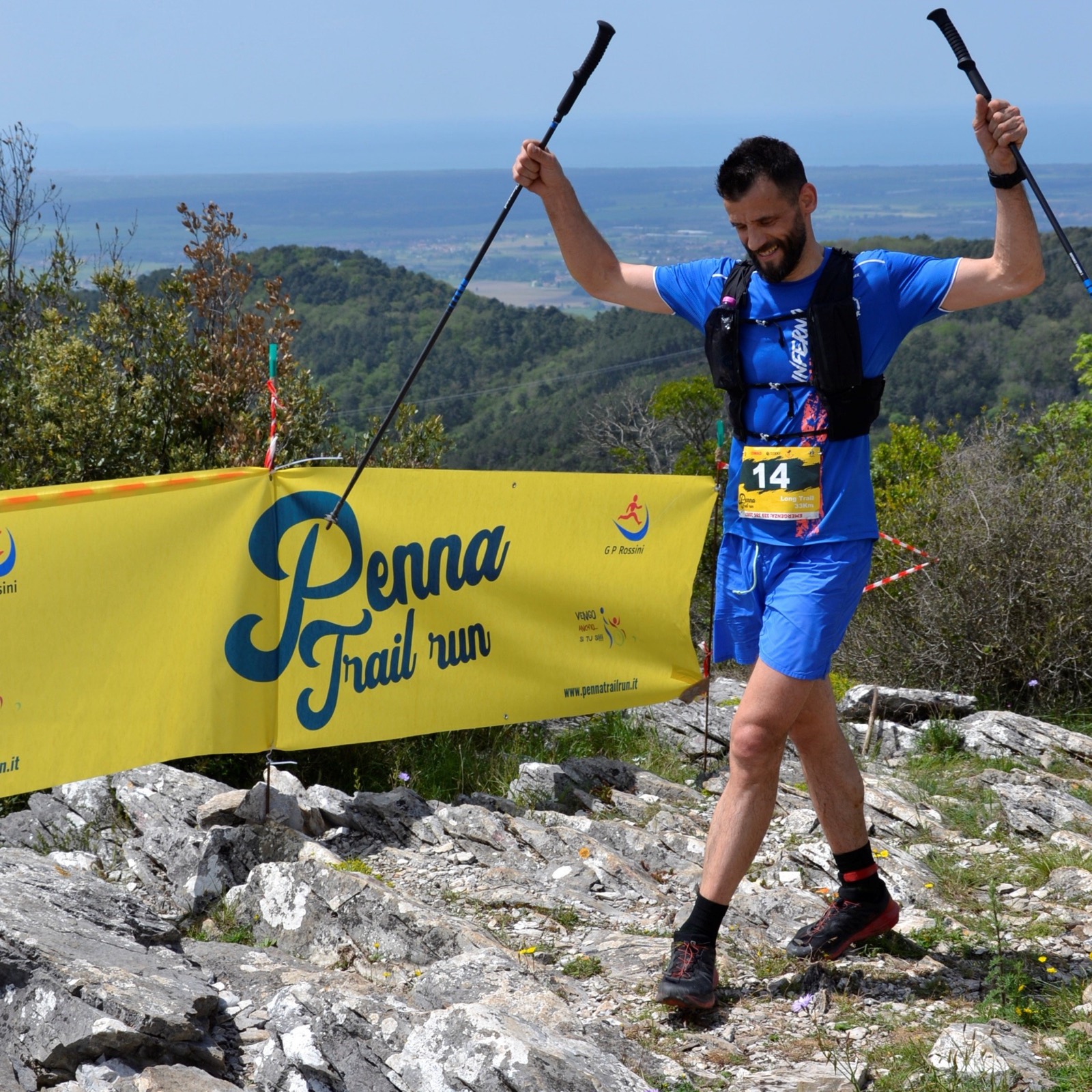 Atleta esulta in vetta con i bastoncini alzati davanti allo striscione Penna Trail Run